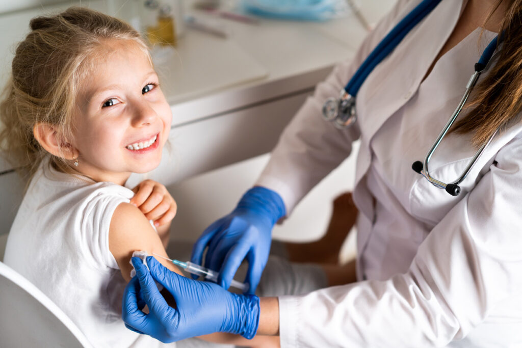 Niña sonriente mientras le inyectan la vacuna de la gripe en una consulta
